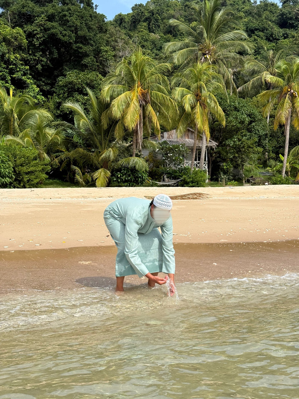 Un qamis vert d'eau au bord de la mer, les mains dans l'eau.